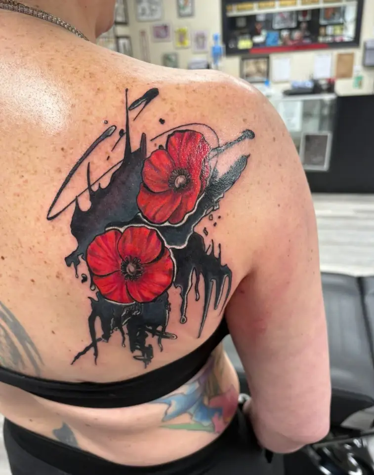 Red poppy flowers with black ink splash tattoo on the shoulder blade