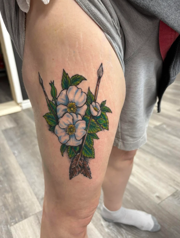 White wild roses with crossed arrows color tattoo on the thigh